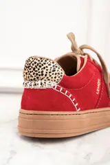 Zapatillas rojas de gamuza con cordones color beige y suela marrón. Detalle de animal print en el talón y pespuntes blancos.