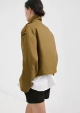Chaqueta corta de lino color verde militar, con cuello solapa ancho, doble botonadura frontal y bolsillos laterales.
