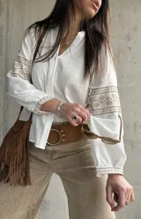 Camisa blanca de calce relajado y tejido liviano, con escote en V y delicados detalles bordados geométricos en tonos tostados en las mangas abullonadas y puños.