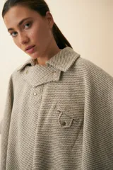 Poncho de lana fina sin teñir, con cuello camisero, cartera con broches a presión y bolsillo ojal. Diseño de estilo campestre con textura tejida.