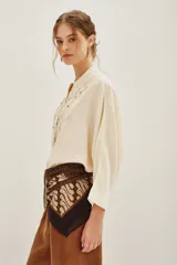 Camisa de viscosa color crema, con cuello mao y cierre frontal de botones. Presenta un delicado bordado floral en el frente y mangas tres cuartos con puños rectos.