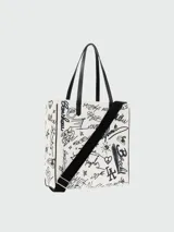 Bolso tipo tote de lona color crudo con estampado de grafitis en negro y asas de cuero negro.