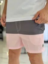 Short de baño con diseño bicolor en tonos gris y rosado, con costuras decorativas visibles en contraste y pequeño aplique circular en el lateral.