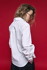 Camisa blanca de manga larga con volumen y estructura, cierre frontal con botones y lazo ajustable en la cintura que realza la silueta.