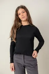 Polera de manga larga color negro, con textura acanalada, cuello redondo y terminaciones con volados en el cuello, puños y ruedo.
