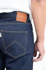 Jean clásico de corte recto, cinco bolsillos, color azul oscuro. Confeccionado en denim de 14 onzas sin elastano, con botones de cobre y costuras color camel.