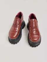 Mocasines de cuero con textura de reptil en color bordó, con plataforma dentada negra y detalle de diseño calado en la solapa delantera.