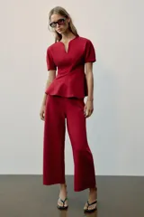 Top peplum confeccionado en hilatura de algodón de color bordó, con escote en V pronunciado, mangas cortas abullonadas y bajo con vuelo.