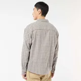 Camisa de manga larga con estampado de cuadros en tonos beige y marrón, confeccionada en franela de algodón. Presenta cuello clásico, cierre frontal con botones y un bolsillo en el pecho.