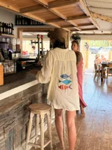 Camisa oversize de lino a rayas blancas y rosadas, con mangas largas y diseño bordado de peces en la espalda.
