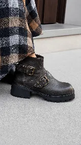 Bota corta de cuero con acabado desgastado, suela track robusta y doble correa con hebillas metálicas laterales.
