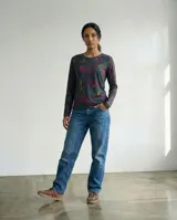 Remera de manga larga en jersey con estampado de líneas orgánicas en tonos verdes, violetas y naranjas. Presenta un corte recto y cuello redondo, diseñada para un ajuste cómodo y versátil.