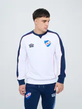 Buzo deportivo azul marino con detalles en rojo y blanco en cuello, hombros y mangas, de cuello redondo y manga larga, con el logo de Umbro y el escudo del Club Nacional de Football bordados en el pecho.