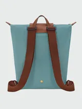 Mochila de diseño minimalista en color beige, con solapa y asa superior en cuero marrón texturizado. Cuenta con correas ajustables en color marrón y cierre principal.