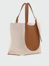 Bolso tote XL Longchamp modelo Complice, confeccionado en lona color crudo con detalles de cuero marrón en las asas y en un bolsillo frontal semicircular.