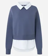 Buzo azul de corte amplio confeccionado en mezcla de algodón y poliéster, con diseño superpuesto que incluye cuello clásico y dobladillo en tono contrastante simulando una camisa por debajo.