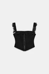 Top corsetero negro de escote recto con tirantes anchos, detalle de encaje con volados en el escote y los tirantes, y cierre frontal con ganchos metálicos.