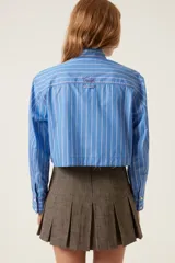 Camisa corta celeste a rayas blancas con bordes sin rematar, bolsillos de parche con solapa y pines removibles con motivos de Jamaica.