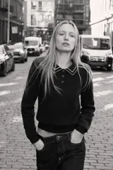 Jersey de punto color azul marino, de manga larga, con cuello polo y cierre frontal de botones. Presenta vivos blancos con borde ondulado en el cuello, puños y ruedo inferior.