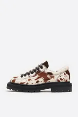 Zapato de cuero con acabado de pelo y estampado animal print tipo vaca, con punta redonda, cierre de cordones y suela track de goma negra.