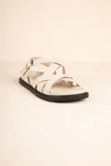 Sandalia baja de tiras cruzadas color camel, con hebilla metálica ajustable en el tobillo y suela negra gruesa.