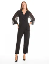 Enterito de seda fría color negro, con escote en V cruzado y cintura elástica con lazo lateral. Presenta mangas largas de gasa transparente con puños elásticos fruncidos y pantalón de corte recto al tobillo.