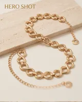 Cinto de metal dorado con eslabones entrelazados en forma de ocho y una cadena colgante fina con un dije circular en el extremo.