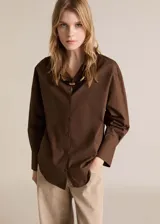Camisa de corte regular fit en color marrón chocolate, confeccionada en tejido de algodón. Presenta cuello camisero clásico, cierre frontal con botones y mangas largas con puños abotonados.