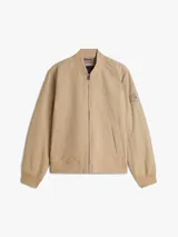 Campera estilo bomber Tommy Hilfiger color beige, con cierre frontal de cremallera, bolsillos laterales de ojal, puños y dobladillo de canalé. Cuenta con el logotipo de la marca bordado en el pecho y un parche distintivo en la manga.