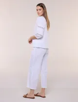 Blusa blanca de calce suelto y caída ligera, con escote en V y cuello Mao pequeño. Presenta mangas tres cuartos abullonadas con elástico en los puños y detalles de calado o puntilla encastrada. Espalda lisa con canesú y leve frunce.