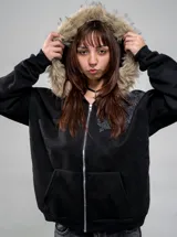 Campera de algodón y poliéster color negro con cierre frontal y capucha con borde de piel sintética. Cuenta con bolsillos frontales estilo canguro y diseño estampado en el pecho.
