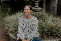 Buzo de tejido de punto calado con diseño de red, cuello redondo y mangas largas abullonadas. Presenta una textura jaspeada en tonos gris y blanco.