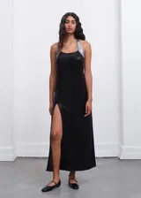 Vestido largo negro de corte recto con escote halter y tirantes brillantes en tono plateado. Presenta un tajo lateral pronunciado en la falda.