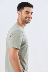 Remera verde pistacho de manga corta y cuello redondo, con diseño gráfico estampado en el frente con inscripciones y tipografías en tonos oscuros y blancos.