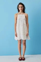 Vestido corto blanco de corte en A, confeccionado en tela con diseño de broderie floral y bordes scalloped. Cuenta con escote cuadrado y tirantes finos.