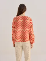 Camisa voluminosa de algodón con mangas amplias y abullonadas que se ajustan en los puños. Tiene calce suelto, hombro caído, cuello redondo y cierre frontal con botones. Presenta estampado geométrico en tonos mostaza y beige.