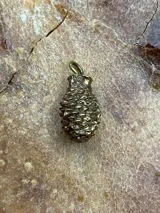 Dije de bronce con forma de piña, modelado y tallado a mano. Incluye argolla para colgar.