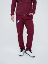 Pantalón deportivo de hombre Umbro del Club Nacional de Football, modelo Grok, de color bordó. Presenta escudo del club en una pierna y logo de Umbro en la otra.