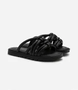 Sandalia plana de color negro con diseño de tiras tubulares acolchadas tipo puffer entrelazadas con nudos. Presenta puntera redonda, plantilla anatómica y suela de goma al tono.