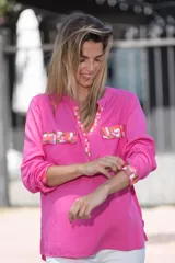 Camisa fucsia de viscosa con detalles pintados a mano en cobre, rosa y blanco en cuello, bolsillos y puños. Presenta mangas largas, cuello en V con escote abotonado y bolsillos frontales con solapa.
