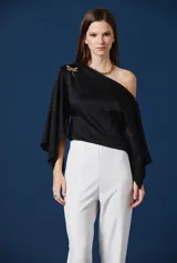 Blusa negra de satén con diseño asimétrico de un solo hombro y mangas amplias tipo capa. Presenta un aplique decorativo en forma de libélula sobre el hombro.