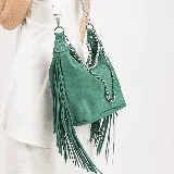 Bolso bandolera verde de cuero vacuno con flecos largos. Tiene dos bolsillos con cierre en la parte trasera, cierre superior, forro interior con bolsillo con cierre y bolsillo para el móvil. Incluye dos correas removibles: una de cuero ajustable y otra de cadena.