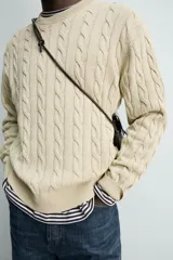 Sweater de punto con diseño de trenzas, color beige, cuello redondo y manga larga con terminaciones en rib.