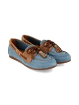 Mocasín estilo náutico confeccionado en cuero y gamuza, en tono celeste y detalles marrón tostado, con cordones de cuero, ojales metálicos dorados y borlas decorativas en el empeine.