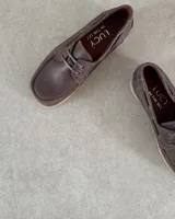 Zapato náutico de cuero vacuno color marrón con cordones y suela clara.