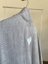 Ruana de tela tipo tapiz con textura, en color gris. Presenta un diseño abierto con caída estructurada y etiqueta decorativa en el lateral.
