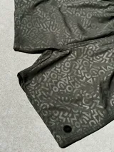 Short de baño verde oliva con estampado de letras y figuras geométricas en tono sobre tono. Cintura elástica negra con cordón blanco.