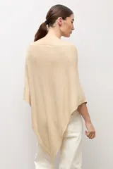 Capa tejida en hilo de lurex color beige, con cuello bote y diseño asimétrico de corte fluido.