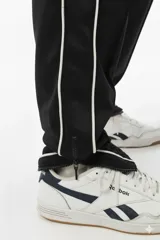Pantalón de jogging negro con vivo lateral doble blanco, corte holgado, tiro medio, botamanga elastizada y cierres en los tobillos.