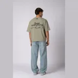 Remera boxy de calce corto y ancho, color verde oliva, con cuello redondo, mangas cortas y estampa frontal minimalista con texto y logo.